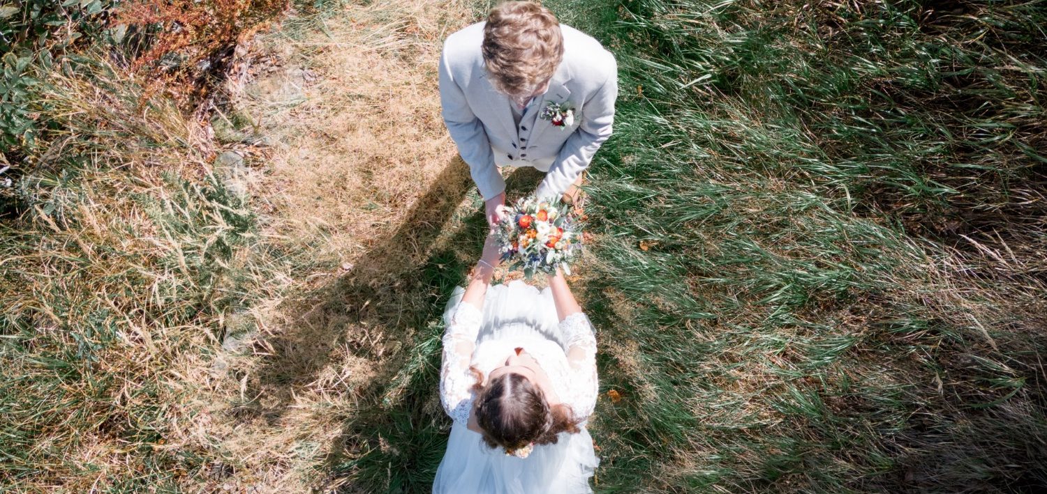 Brautpaar mit Hochzeitsstrauß auf einem Waldweg, von oben fotografiert